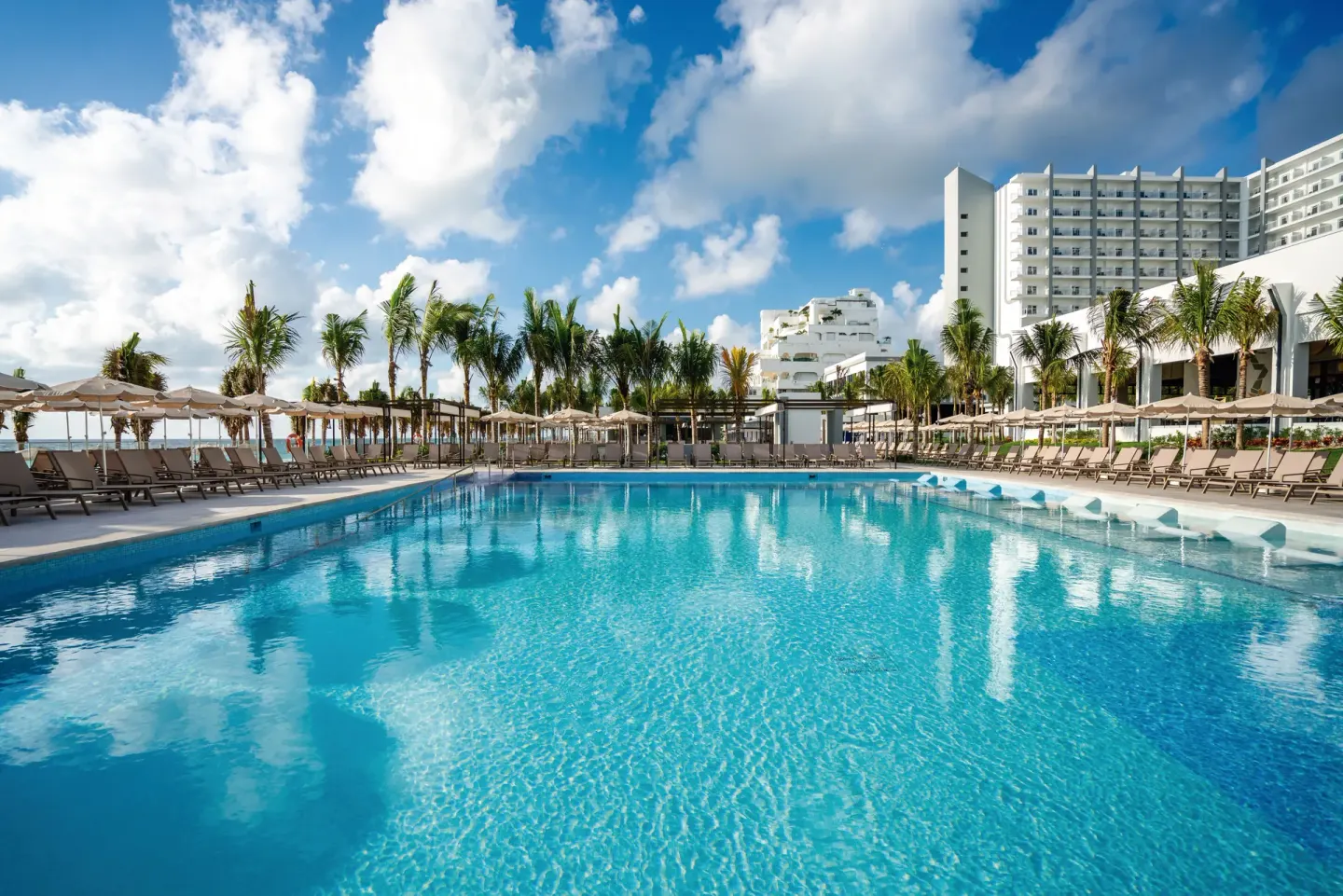 Large resort pool with loungers and palm trees at Hotel Riu Palace Kukulkan.