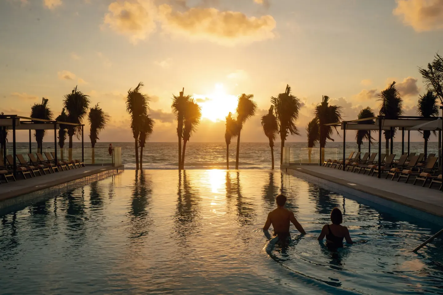 Guests in the pool at sunset overlooking the ocean at Hotel Riu Palace Kukulkan.