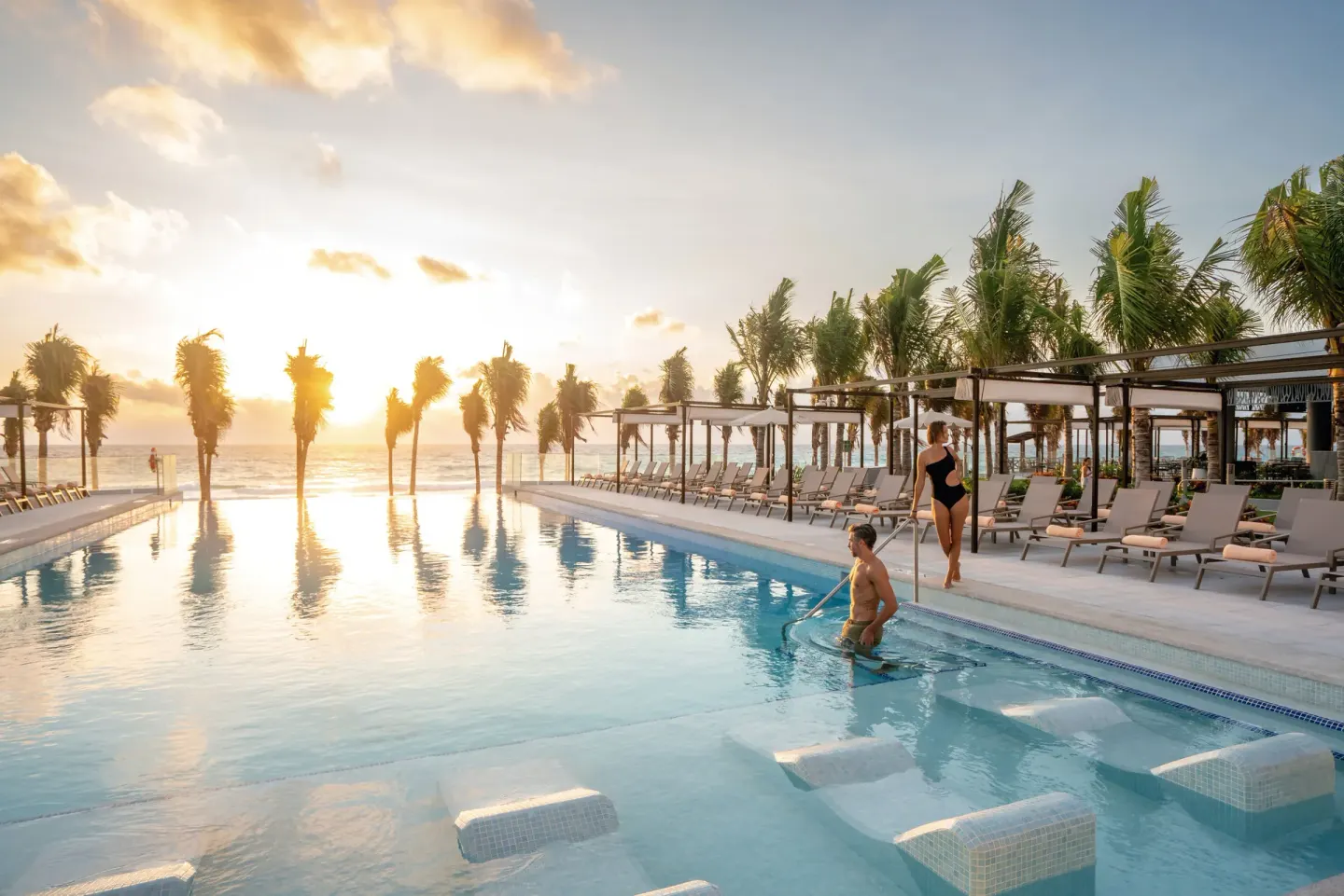 Pool steps, submerged loungers, and guests at sunset at Hotel Riu Palace Kukulkan.