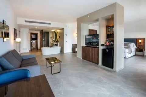 Open-plan Elite Club Suite at Hotel Riu Palace Kukulkan with sofa, tub, TV, minibar, and bed area.