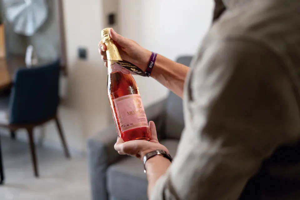 Guest holding a chilled sparkling wine bottle in a suite at Hotel Riu Palace Kukulkan.