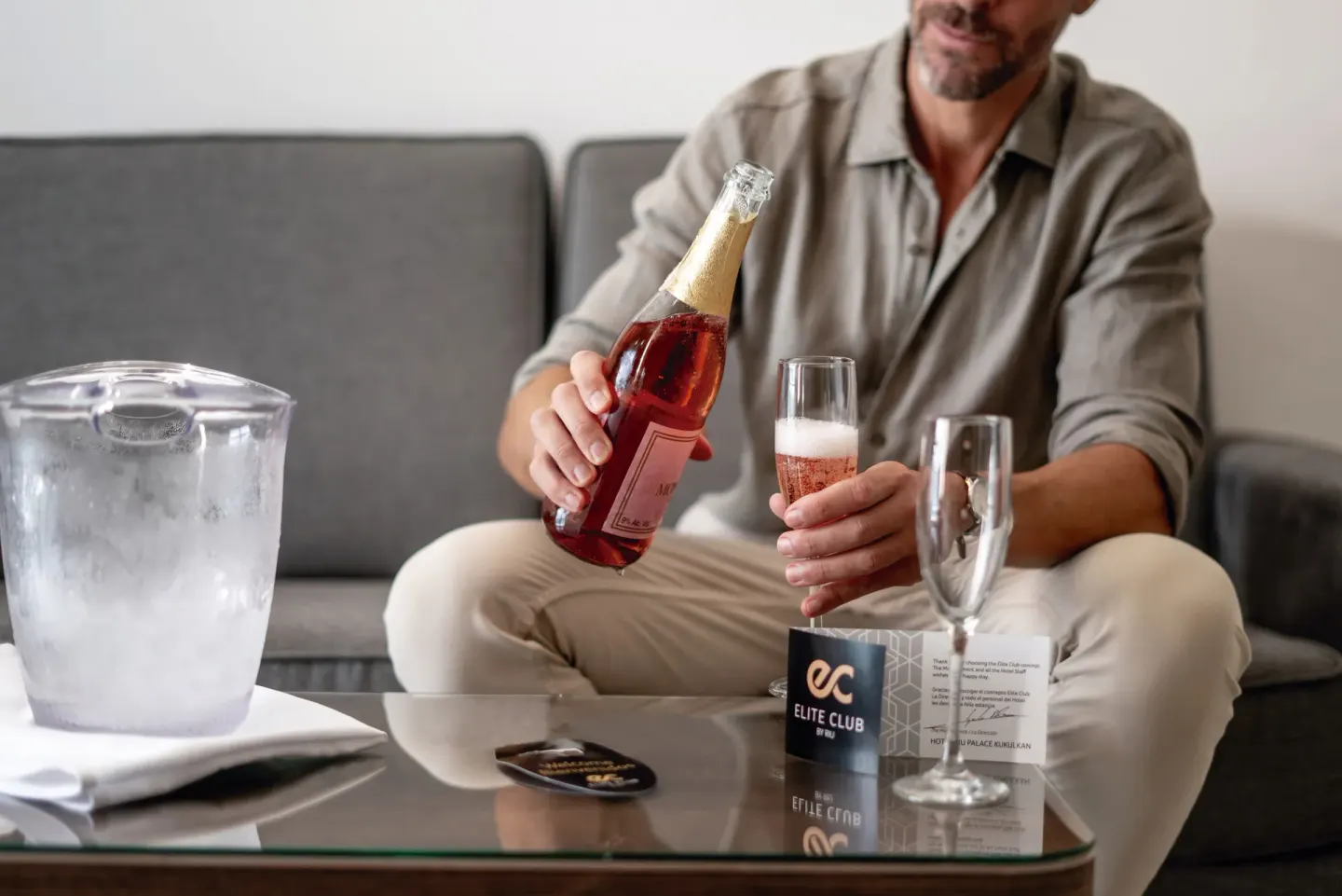 Guest pouring sparkling wine beside an ice bucket in a suite at Hotel Riu Palace Kukulkan.