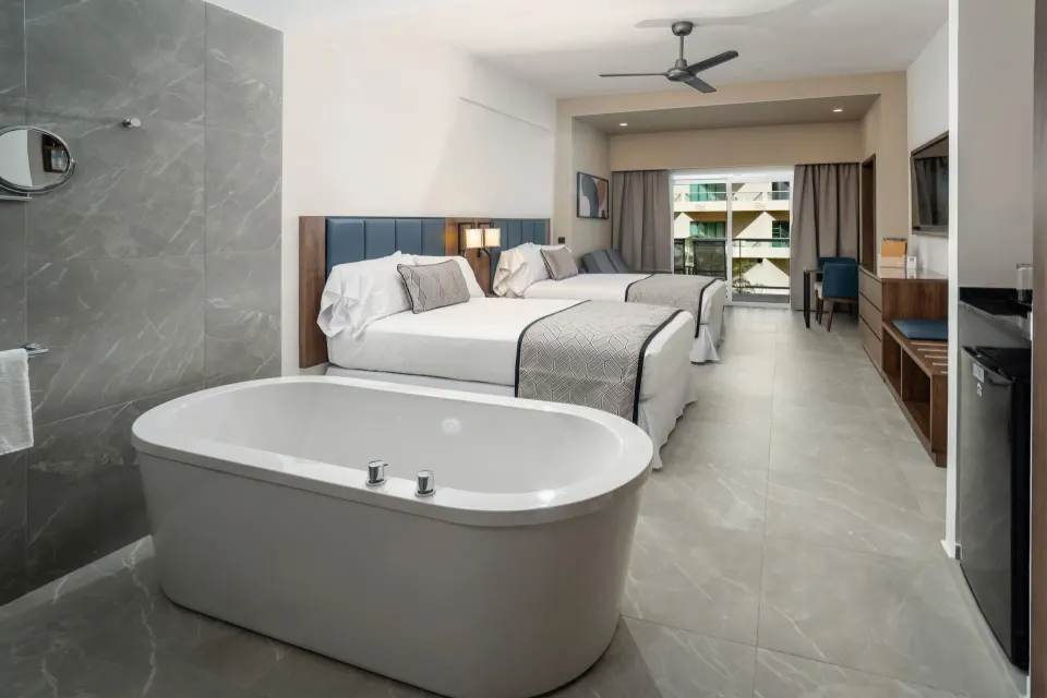 Junior Suite at Hotel Riu Palace Kukulkan with tub, two beds, balcony doors, and TV wall.