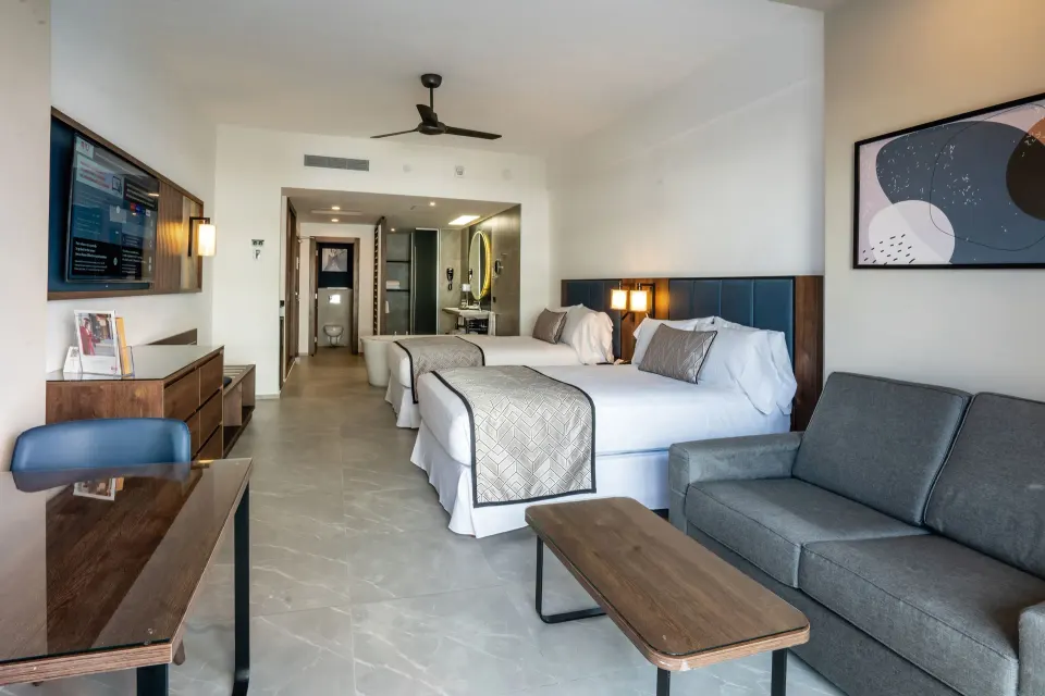 Junior Suite at Hotel Riu Palace Kukulkan with two beds, sofa, desk, and open bathroom beyond.