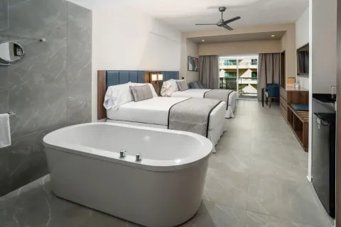 Junior Suite with freestanding tub, two beds, and balcony doors at Hotel Riu Palace Kukulkan.