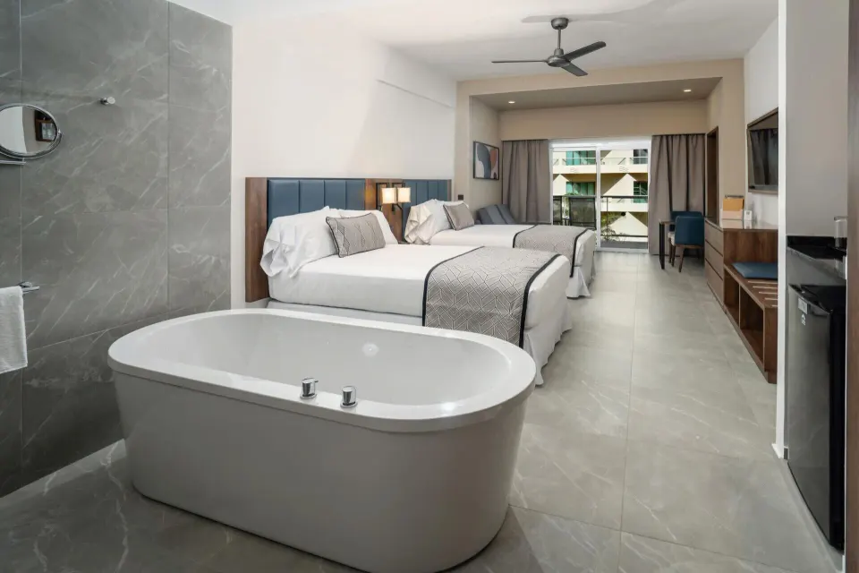 Junior Suite with freestanding tub, two beds, and balcony doors at Hotel Riu Palace Kukulkan.