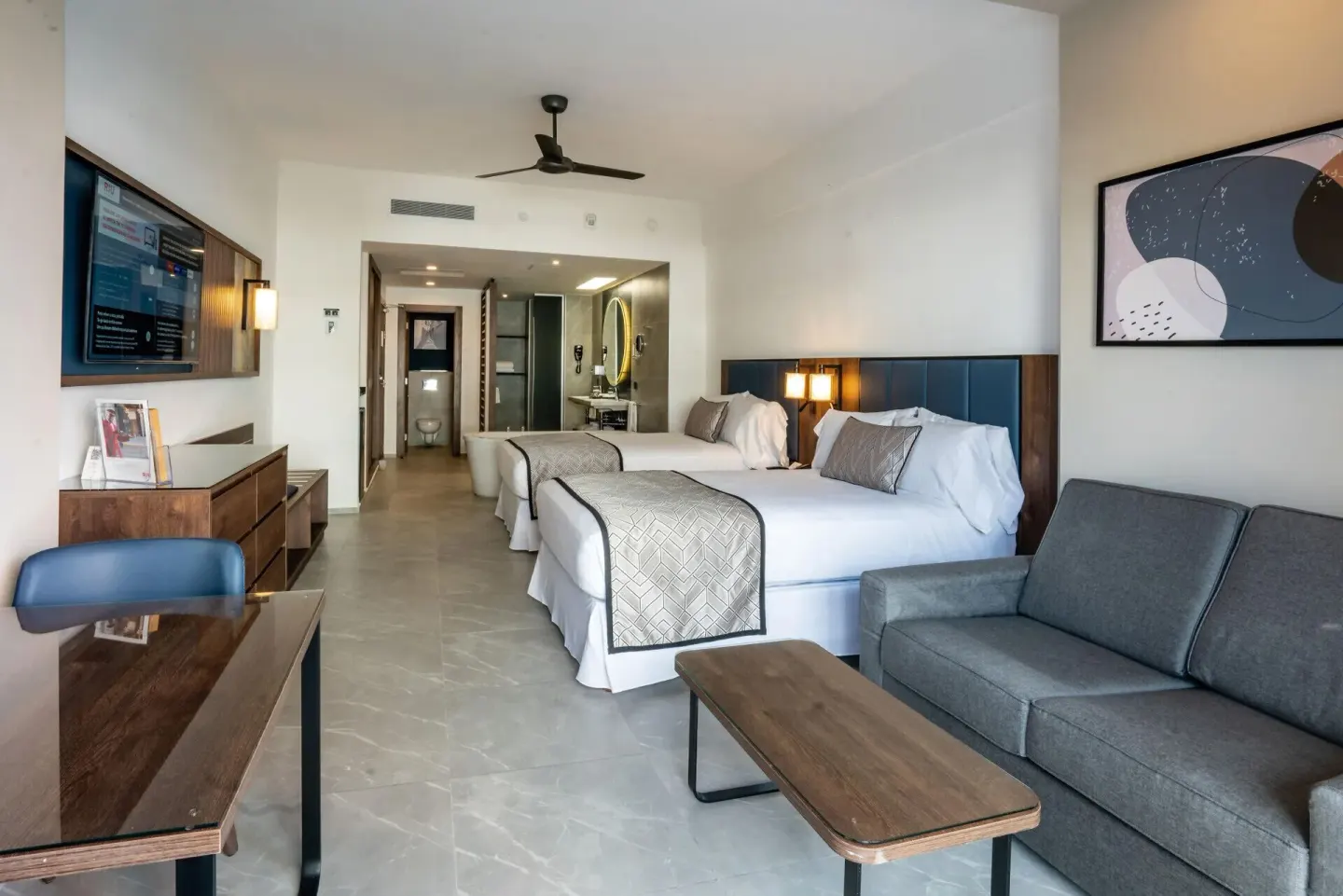 Junior Suite with two beds, sofa, desk, and open bathroom view at Hotel Riu Palace Kukulkan.