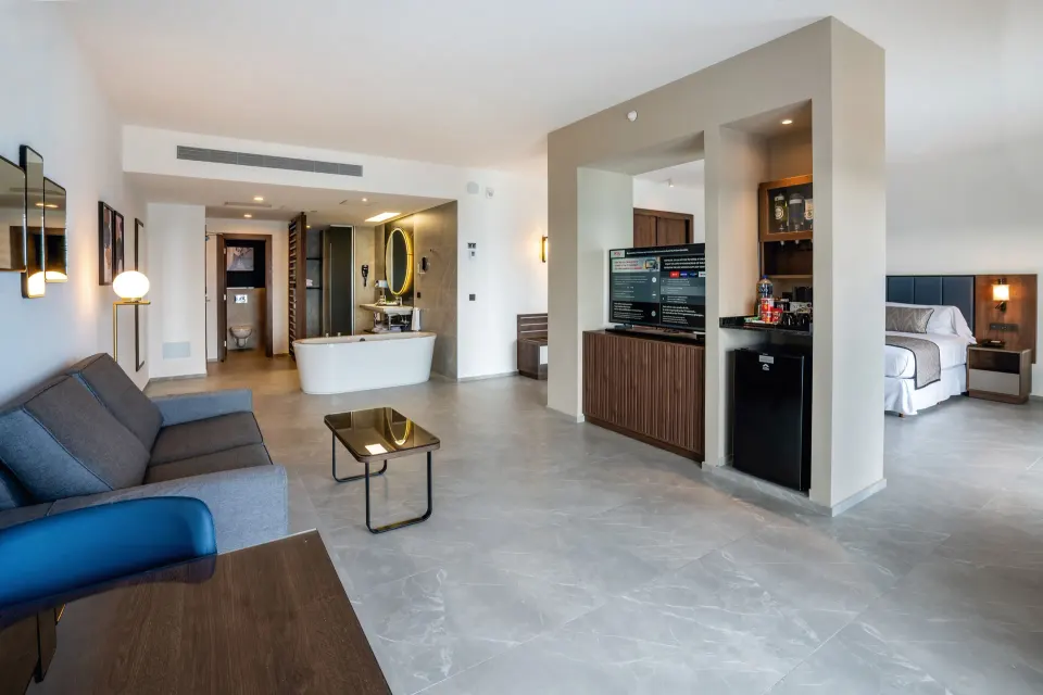 Suite Ocean View Elite Club lounge with TV, minibar area and bed at Hotel Riu Palace Kukulkan.