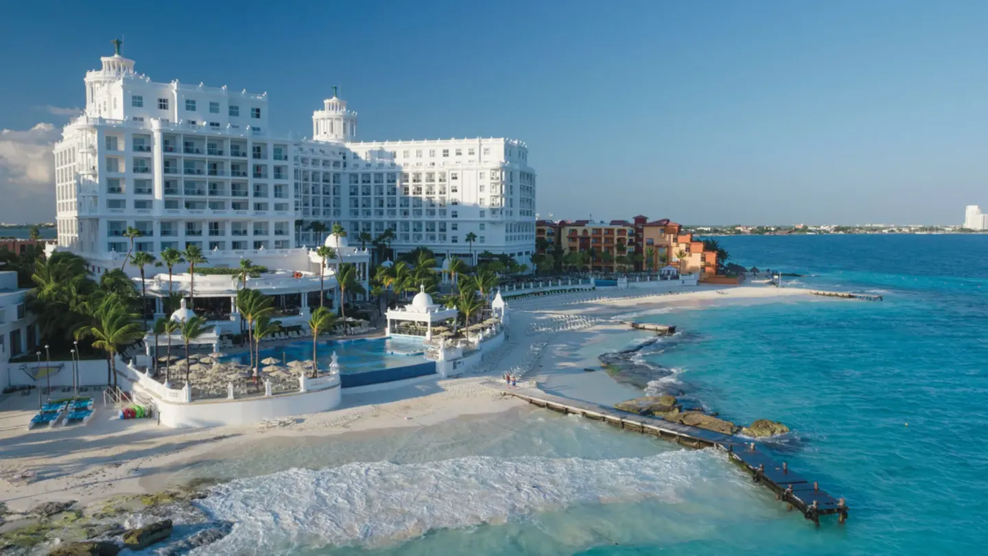 Aerial view of the beachfront, turquoise water, and white resort building at Hotel Riu Palace Las Americas.