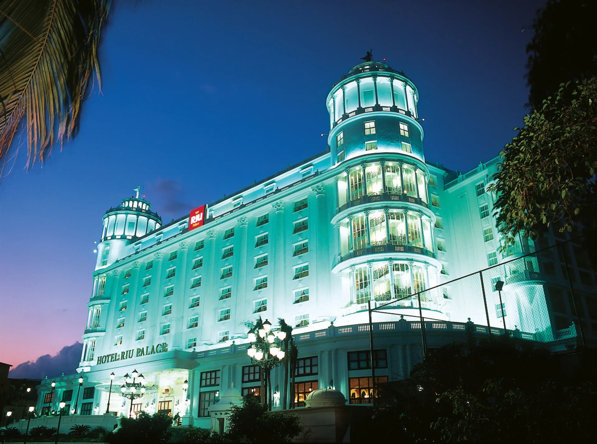 Illuminated exterior facade of Hotel Riu Palace Las Americas at dusk.