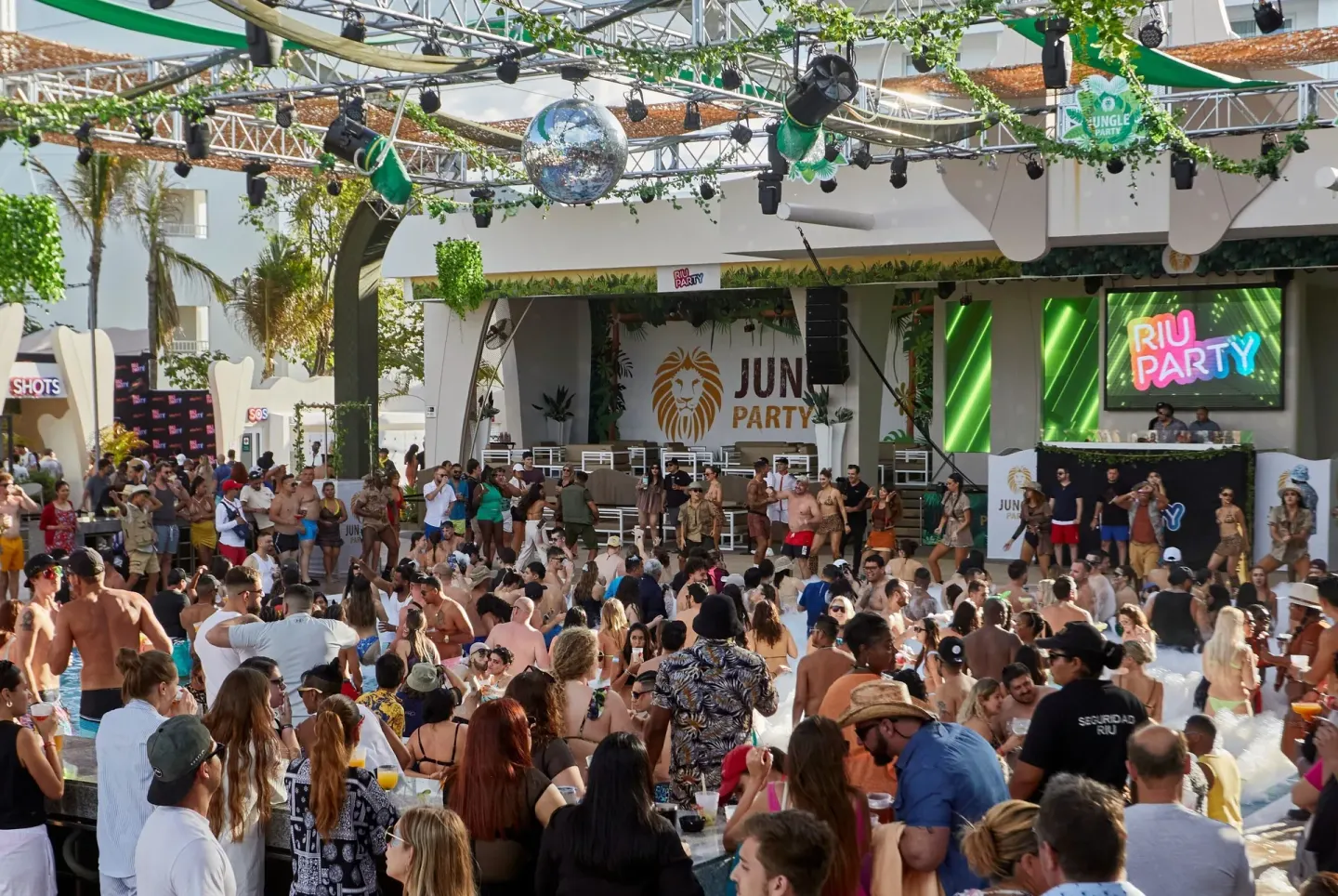 A large outdoor crowd gathers for a pool party at Hotel Riu Palace Las Americas.