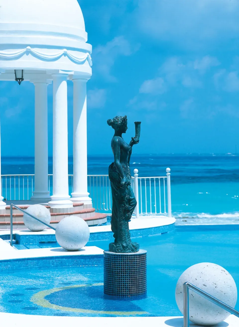 Pool statue, white pavilion, and turquoise sea at Hotel Riu Palace Las Americas.