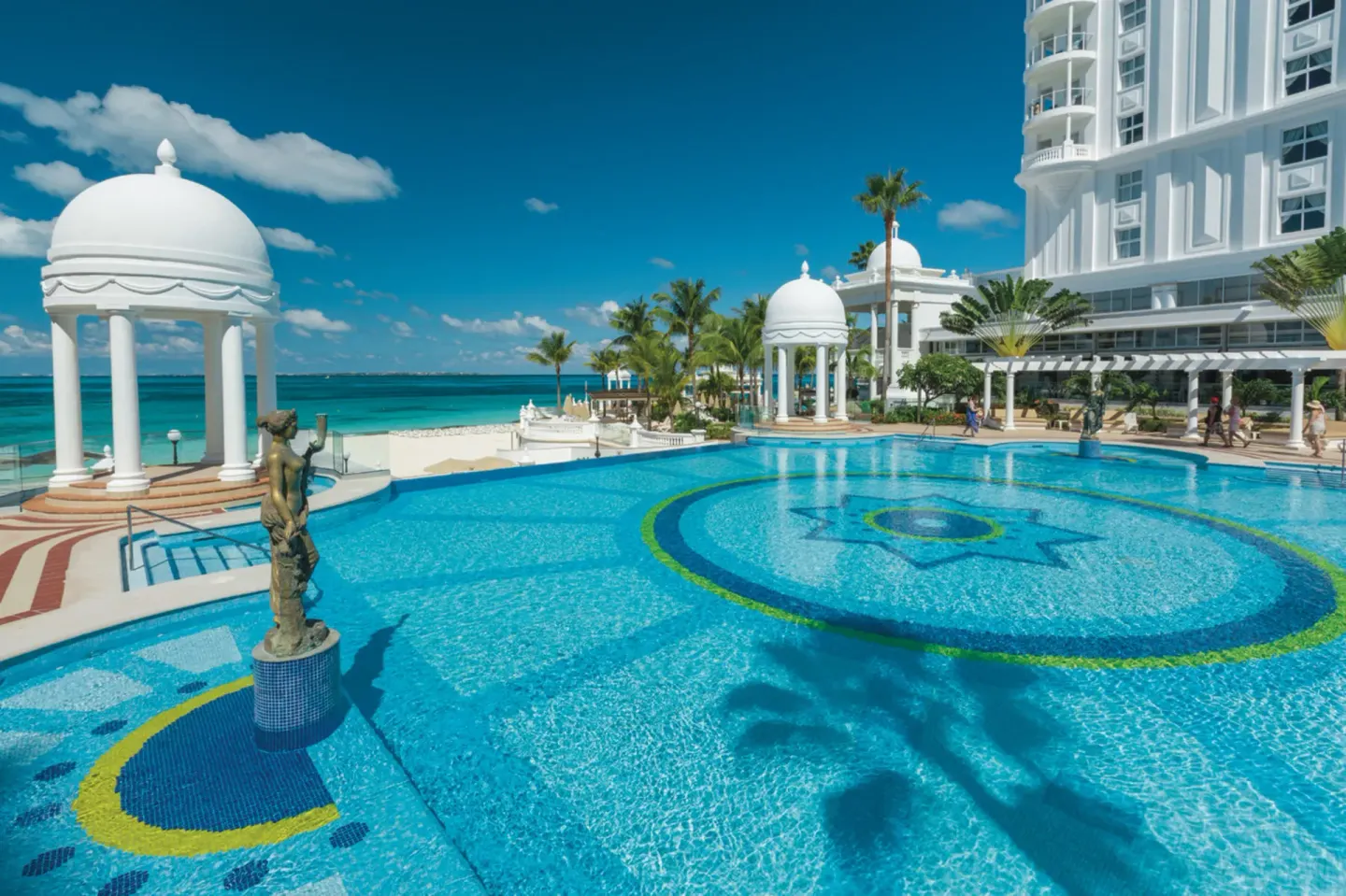 Pool with fountain statue, domed pavilions, and ocean at Hotel Riu Palace Las Americas.