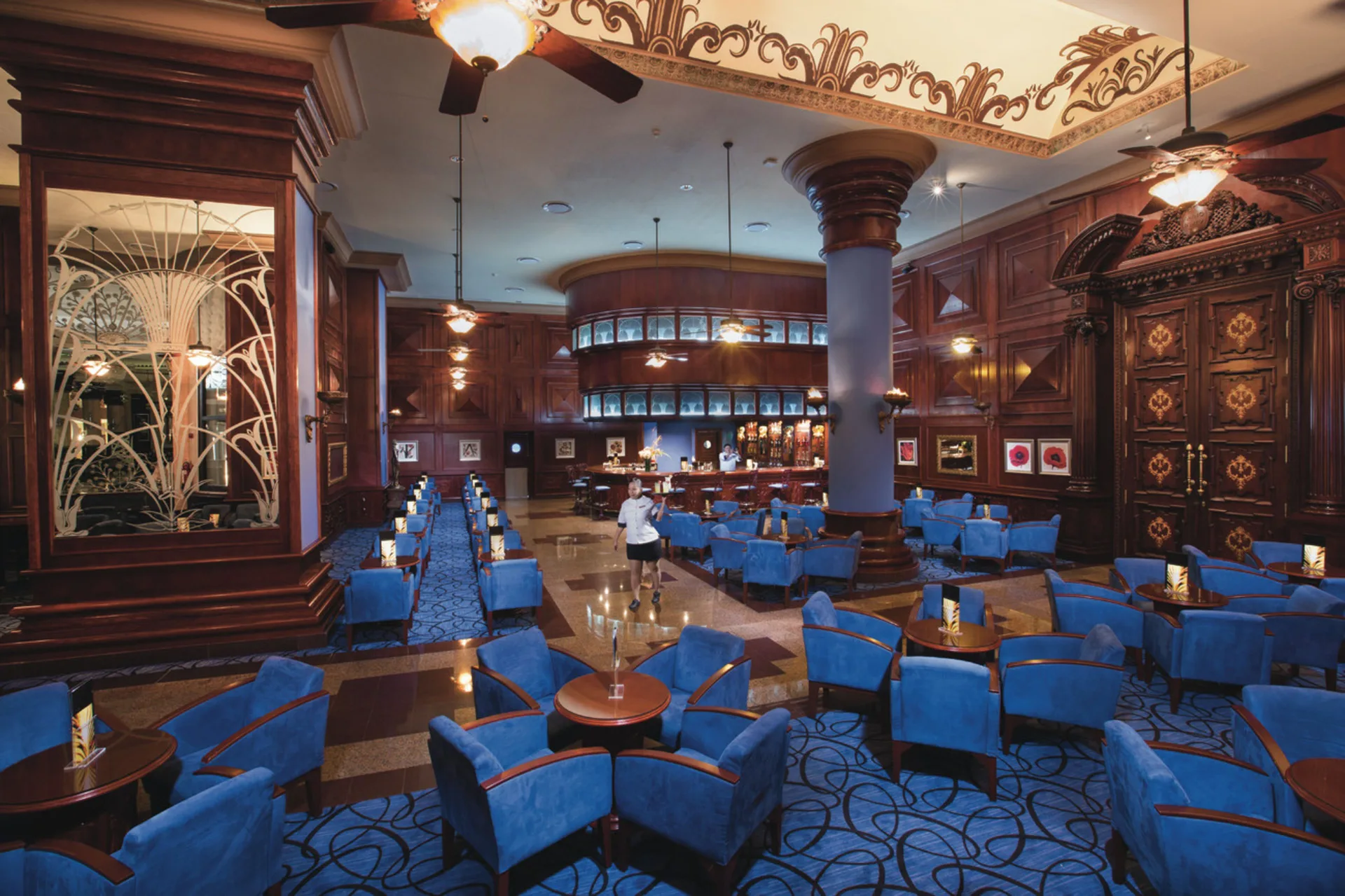 Wood-paneled lobby bar lounge with blue chairs at Hotel Riu Palace Las Americas.
