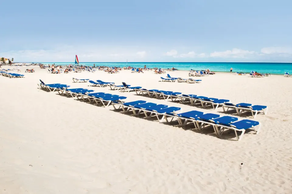Rows of blue lounge chairs on the wide sandy beach at Hotel Riu Palace Mexico