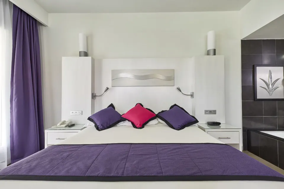 Front view of a king bed with purple accents at Hotel Riu Palace Mexico