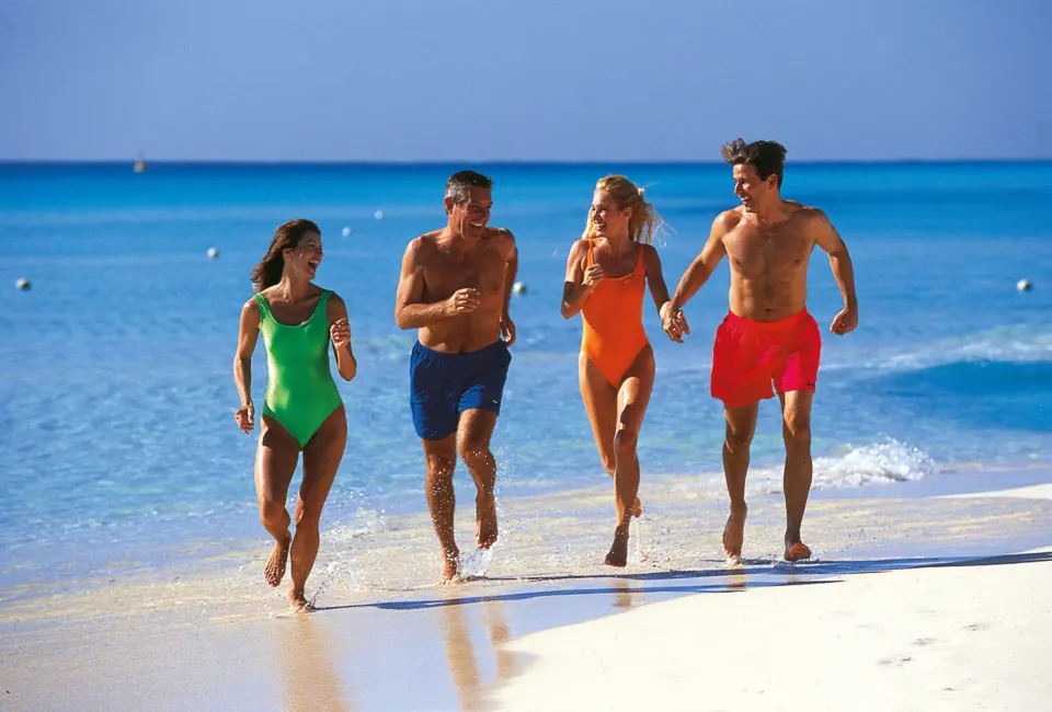 Four people running along a white sand beach with turquoise water at Hotel Riu Palace Mexico