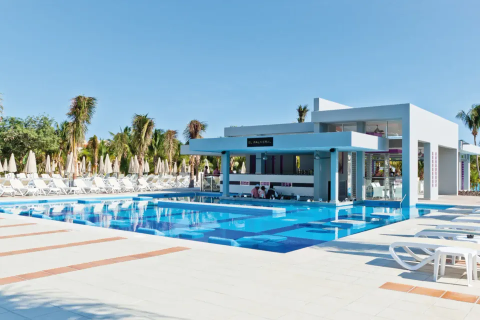 Square pool with many sunbeds and palm trees under a blue sky at Hotel Riu Palace Mexico