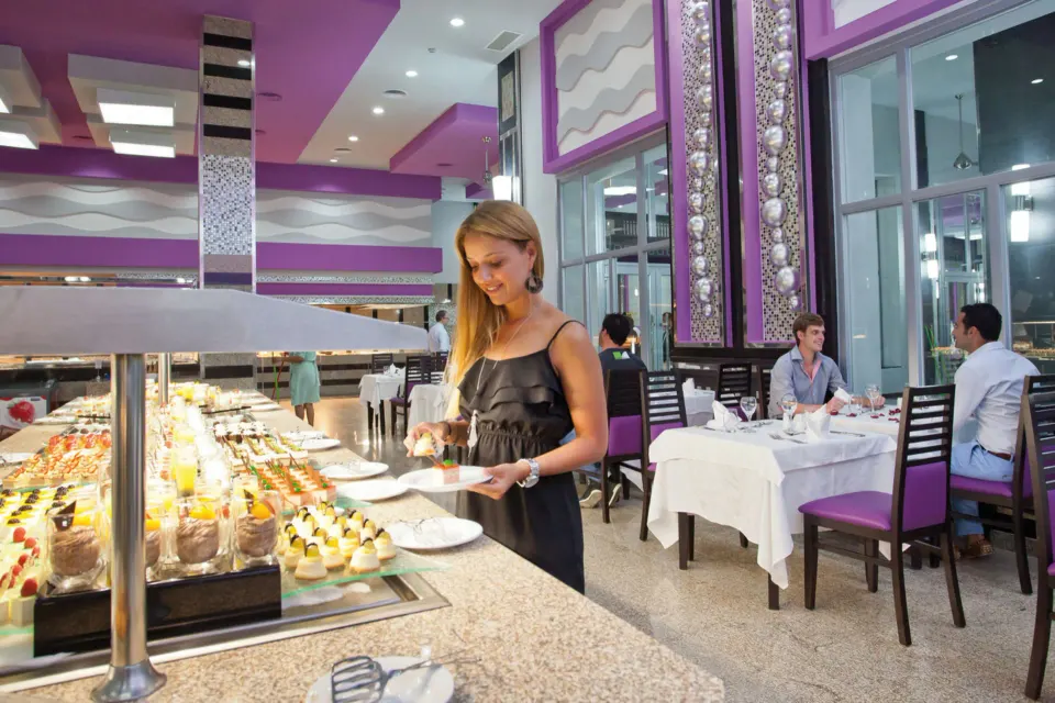 Guest selecting desserts at an indoor buffet in a purple dining room at Hotel Riu Palace Mexico