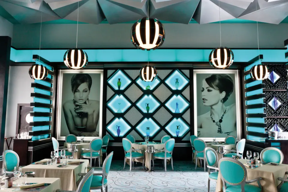 Wide view of a chic turquoise restaurant interior with pendant lights at Hotel Riu Palace Mexico