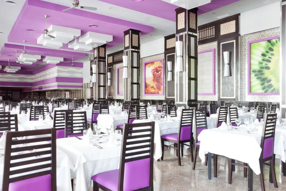 Bright dining room with purple chairs and white table settings at Hotel Riu Palace Mexico