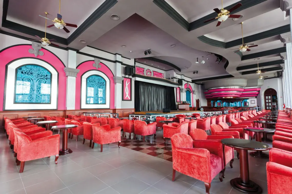 Spacious lounge with rows of red armchairs and a stage at Hotel Riu Palace Mexico