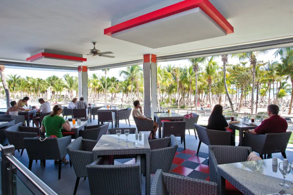 Covered terrace restaurant seating overlooking palm trees and beach at Hotel Riu Palace Mexico
