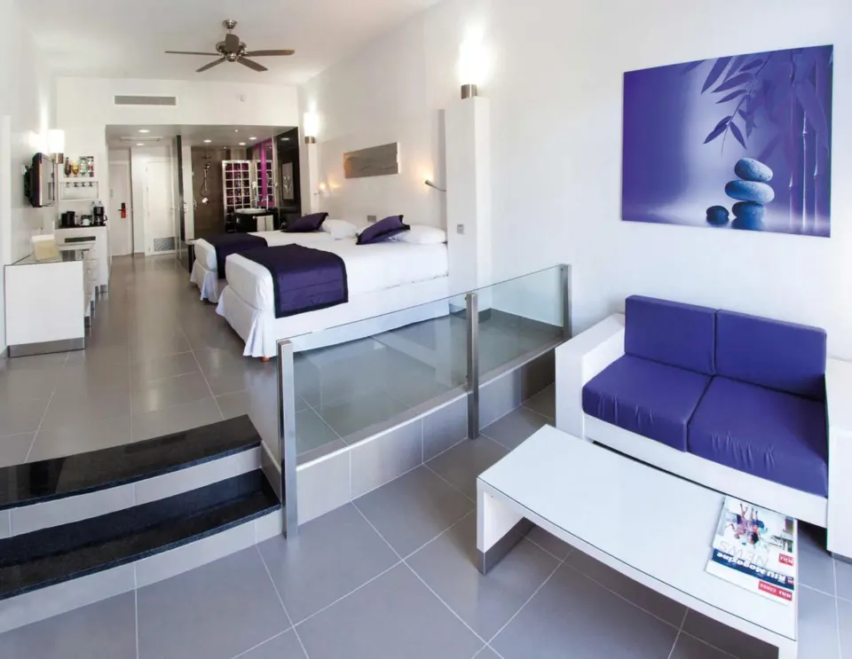 Wide view of Junior Suite Garden View with two beds, sofa seating and vanity area at Hotel Riu Palace Mexico