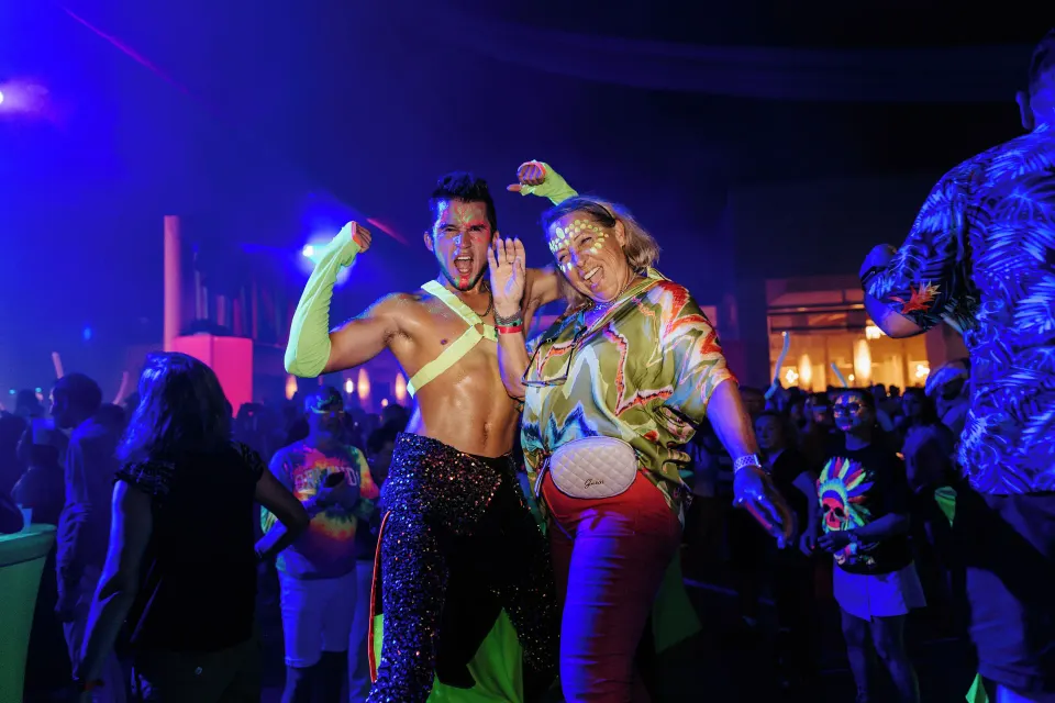 Two costumed dancers posing among partygoers during a neon event at Hotel Riu Palace Mexico