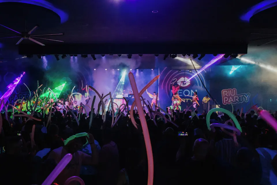 Packed audience waving glow stick balloons at a stage party at Hotel Riu Palace Mexico
