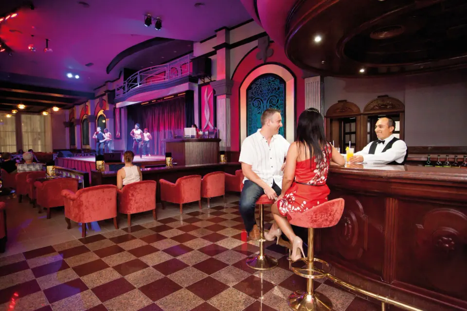 Couple seated at a bar watching live stage entertainment at Hotel Riu Palace Mexico