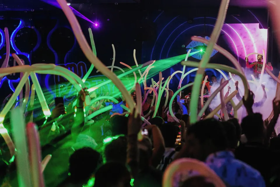 Crowd waving illuminated balloons and green laser beams at an indoor party at Hotel Riu Palace Mexico