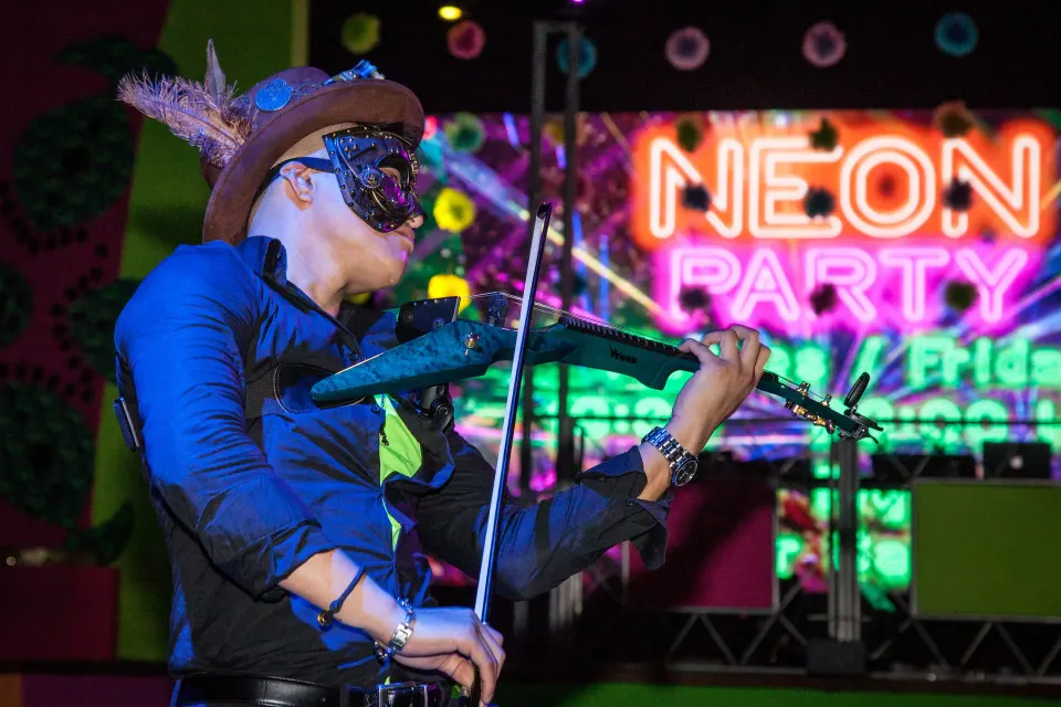 Violinist in a decorative mask playing on stage during a neon party at Hotel Riu Palace Mexico