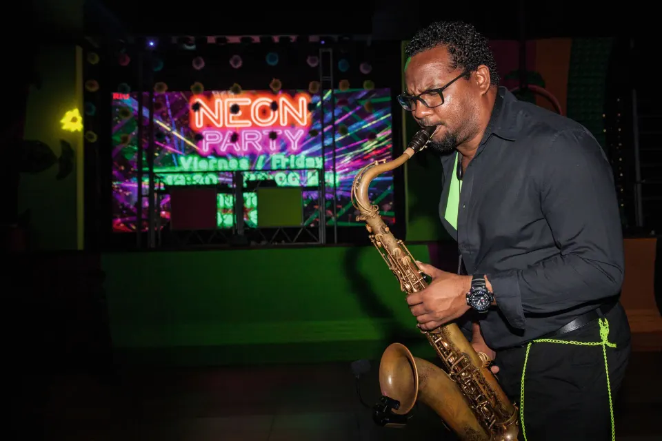Saxophonist performing on stage during a neon-themed show at Hotel Riu Palace Mexico