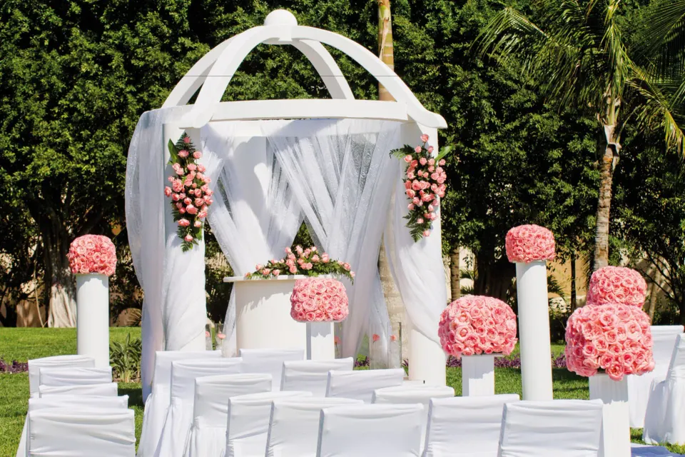 White wedding gazebo with pink floral arrangements on lawn at Hotel Riu Palace Mexico