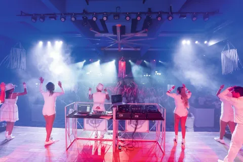 Performers and a DJ face a crowd under stage lights at Hotel Riu Palace Pacifico.