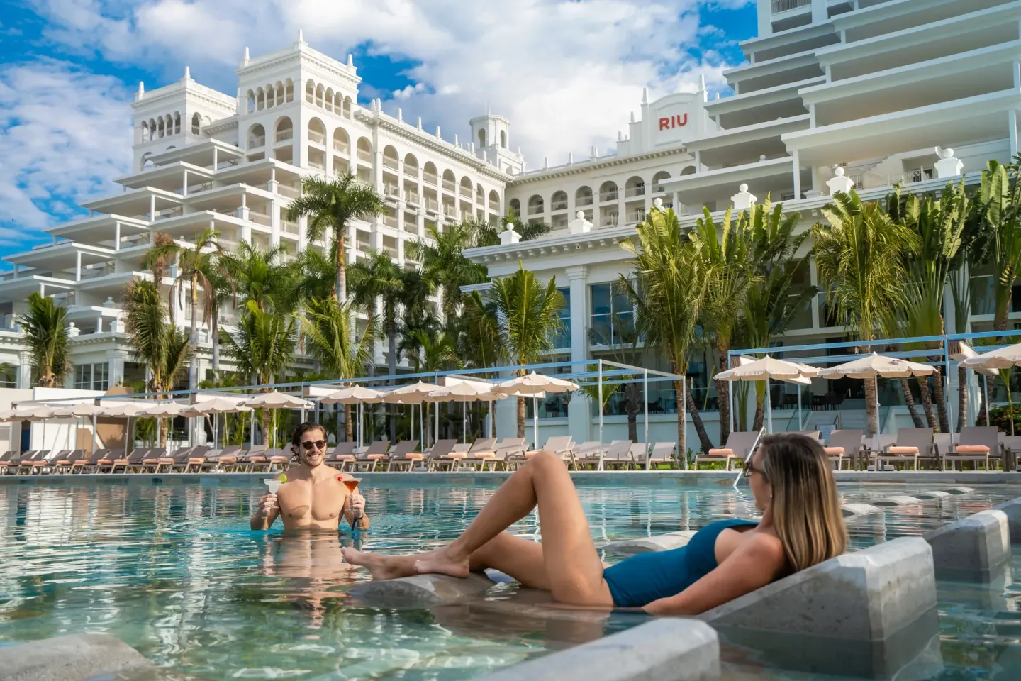 Guests relaxing in the pool with in-water loungers and resort buildings at Hotel Riu Palace Pacifico.