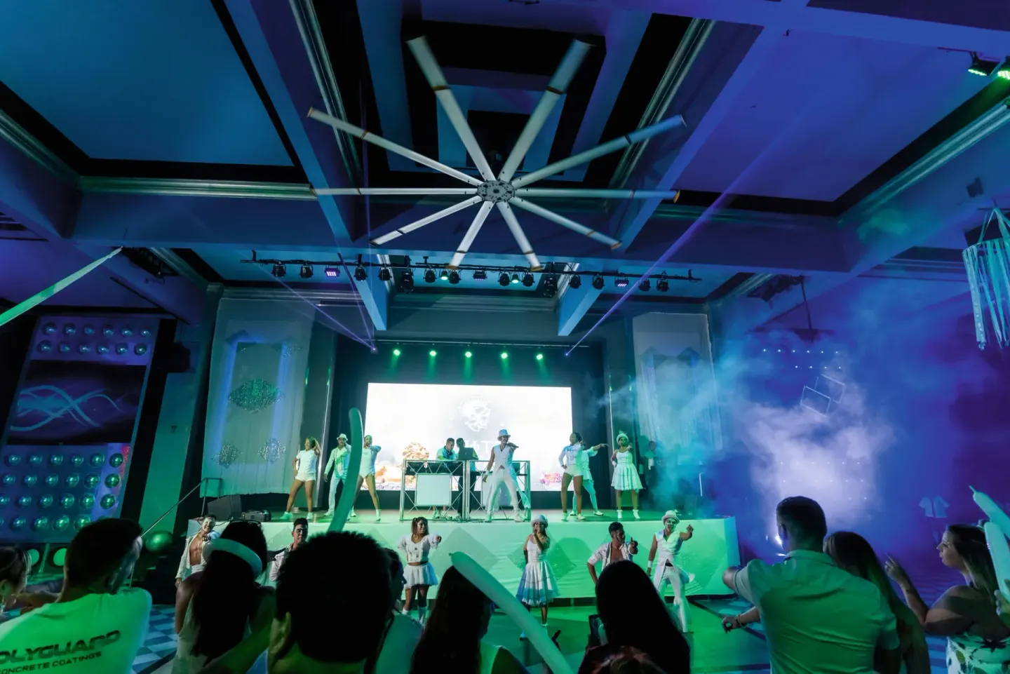 Audience watches a stage party performance with lights and haze at Hotel Riu Palace Pacifico.