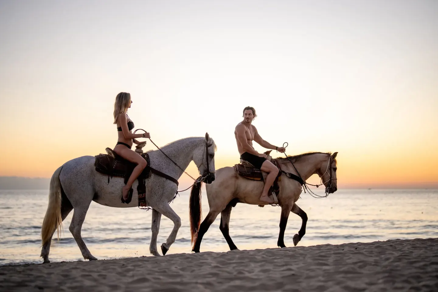 Two guests ride horses along the beach at sunset at Hotel Riu Palace Pacifico.