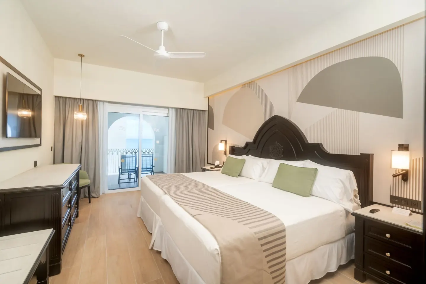 Bedroom of the Junior Suite 2 Bedrooms with bed, dresser, TV, and balcony doors at Hotel Riu Palace Pacifico.