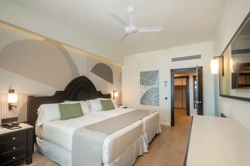 Bedroom of the Junior Suite 2 Bedrooms with bed, ceiling fan, TV, and entry doorway at Hotel Riu Palace Pacifico.