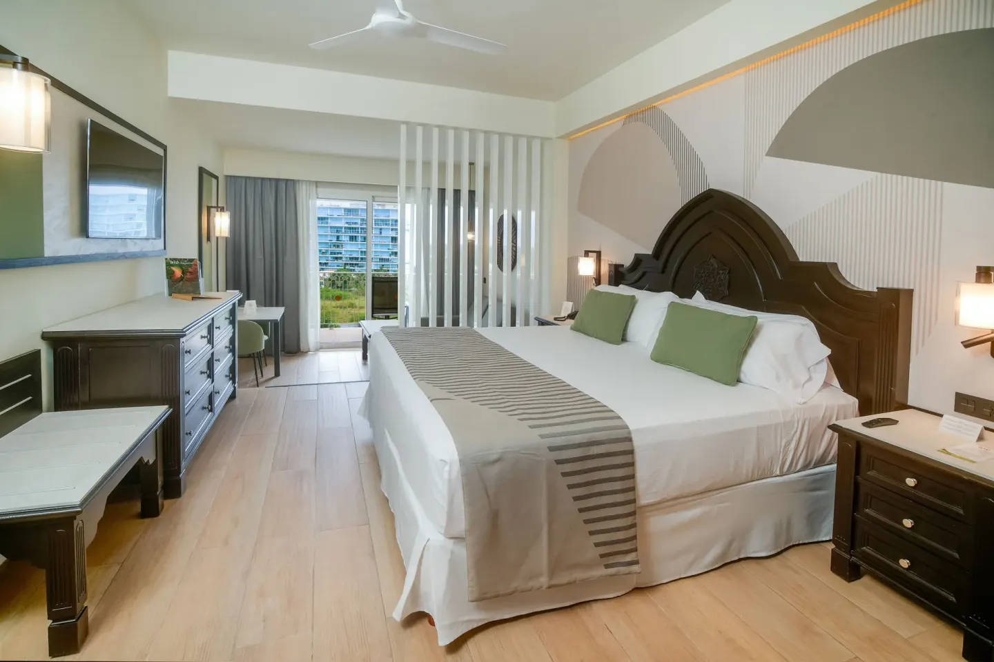 Junior Suite king bed with dresser and balcony doors at Hotel Riu Palace Pacifico.
