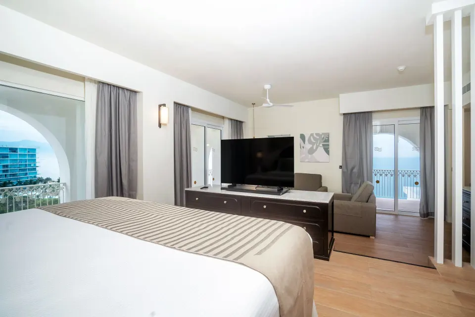 Oceanfront suite bedroom with king bed, TV, sofa, and balcony at Hotel Riu Palace Pacifico.