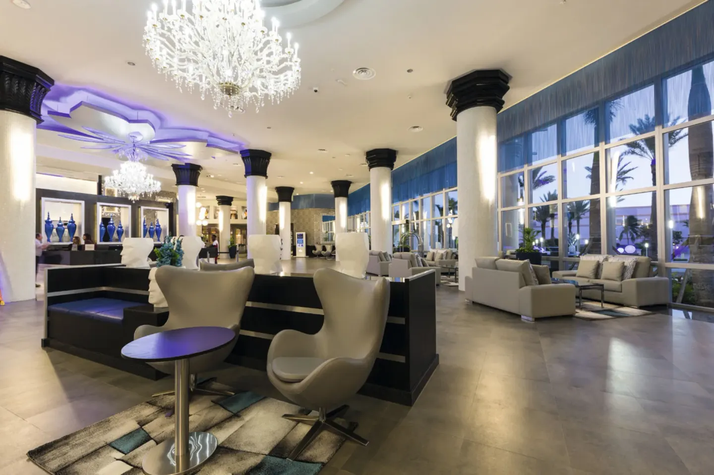 Lobby lounge seating with chandeliers and tall windows at Hotel Riu Palace Paradise Island.