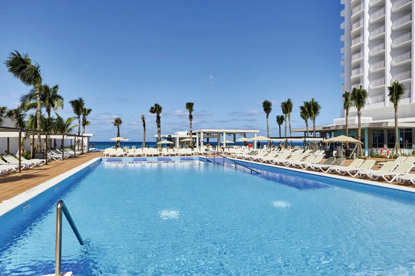 Outdoor pool with loungers, palms, and ocean beyond at Hotel Riu Palace Paradise Island.