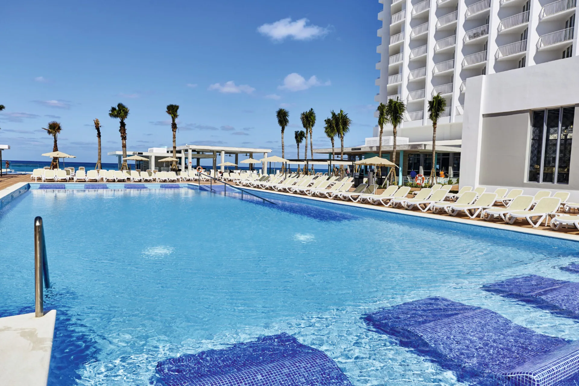 Pool deck with submerged loungers and resort tower at Hotel Riu Palace Paradise Island.