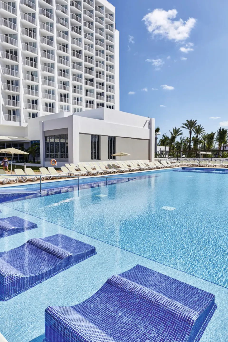 Shallow pool loungers beside the white resort tower at Hotel Riu Palace Paradise Island.
