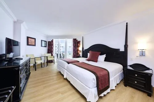 Two beds, dark wood furniture, and balcony doors in a suite at Hotel Riu Palace Paradise Island.