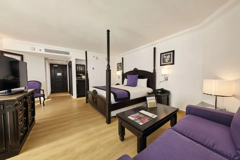 Junior Suite Oceanfront room with four-poster bed and purple seating at Hotel Riu Palace Paradise Island.