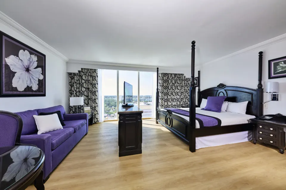 Standard Suite with king bed, purple sofa, and balcony doors at Hotel Riu Palace Paradise Island.